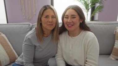 Anne ve kızı sıcak, davetkar bir oturma odasında sıcak bir kanepede oturup sevgi ve mutluluk gösterirken barış jestleri yapıyorlar..