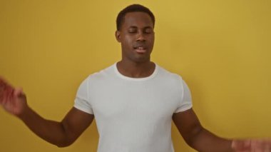 Genç adam, el hareketleriyle, parlak sarı bir arkaplana karşı anlamlı bir şekilde iletişim kuruyor. Basit bir beyaz gömlek içinde kişilik ve tarz gösteriyor..