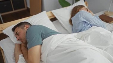 Kadın ve erkek, yatak odasındaki rahat ortamda, ilişki dinamiklerini ve kişisel alanlarını paylaşırken yatakta ayrı yatarlar..