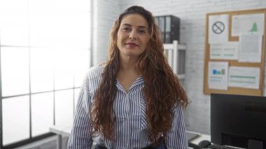 Ofis ortamında gülümseyen bir kadın profesyonel bir görünüm içinde kendine güven ve pozitiflik sergiliyor..