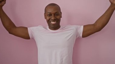 Pembe arka plana karşı kaslarını esnetirken güvenle gülümseyen adam dayanıklılık, pozitiflik ve zindelik gösteriyor..