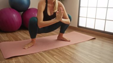 Paspasın üzerinde yoga yapan bir kadın, egzersiz topları ve doğal ışıkla çevrili, sakin bir spor salonu atmosferini yansıtıyor..