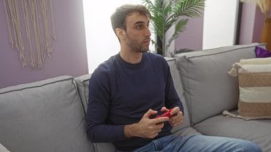 Kadın rahat bir oturma odasındaki kanepede ona sevgiyle sarılırken erkek video oyunları oynuyor.