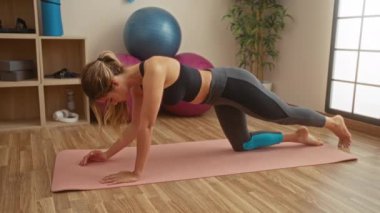 Kapalı spor salonunda spor yapan bir kadın, odaklanarak ve kararlılıkla spor salonu malzemeleriyle çevrili bir şekilde spor yapıyor ve sağlıklı bir yaşam tarzı sağlıyor..