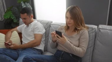 Modern bir oturma odasındaki kanepede akıllı telefonlar kullanan kadın ve erkek rahat ve rahat bir atmosfer yaratıyor ve bitkiler rahat iç mekanı büyütüyor..