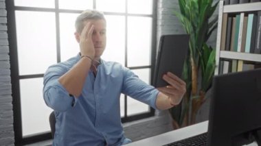 Ofisteki genç adam, modern dekor ve doğal ışık sağlayan geniş bir pencereyle çevrili bir tabletle selfie çekerek ev içi profesyonel atmosferi geliştiriyor..