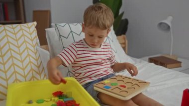 Sarışın çocuk rahat bir yatak odasında eğitici oyuncakla oynuyor.