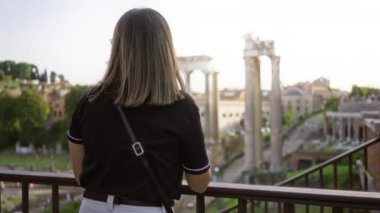 Güneşli bir günde Roma 'daki antik Roma harabelerine ikonik sütunlar ve canlı yeşilliklerle bakan bir kadın..