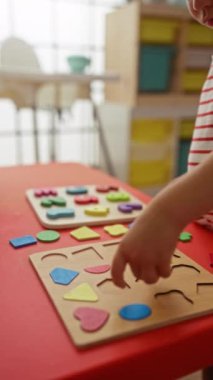 Çocuk, anaokulundaki bir masada renkli geometrik bulmacalarla oynuyor.