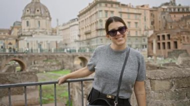 Roma 'da antik mimari, zarif güneş gözlükleri ve bulutlu bir günde sakin bir ifadeyle Roma forumunun keyfini çıkaran kadın, tarihi mirası ve gündelik moda anlayışını ön plana çıkarıyor..