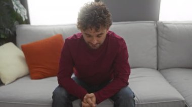 Genç adam parlak bir oturma odasında renkli yastıklarla rahat ve çekici bir hava yayarak rahat bir kanepede oturuyor..