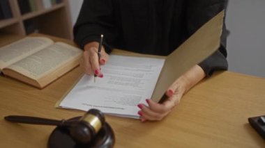 Hukuk belgelerini kalem ve tokmakla inceleyen kadın, mahkeme salonunda masasında açık bir kitapla, yargı ortamı ve karar verme ortamı öneriyor..