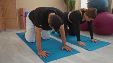 Spor salonundaki paspaslar üzerinde yoga yapan erkek ve kadın modern kapalı alan ortamında spor toplarıyla sağlık ve zindeliğe odaklanıyor..
