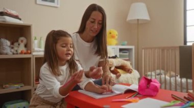 Küçük kızı beşikteki küçük bir masaya resim çizen İspanyol bir kadın oyuncaklarla çevrili, rahat bir evde sıcak bir aile ortamı yaratıyor..