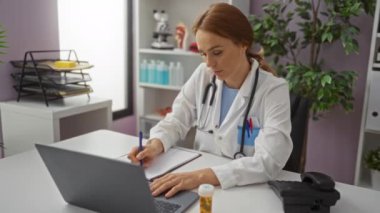 Klinikte çalışan bir kadın doktor dizüstü bilgisayar ve not yazıyor. Etrafı tıbbi malzemelerle çevrili. Profesyonel bir sağlık hizmeti sunuyor..