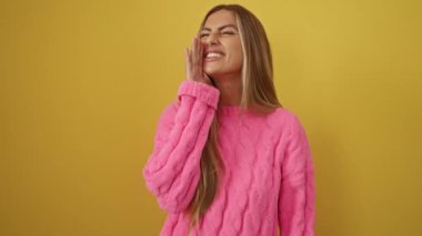 Süveter giyen bir kadın, hiçbir fikri olmayan genç bir sarışın, kolları açık, izole edilmiş sarı arka planda şüpheli.