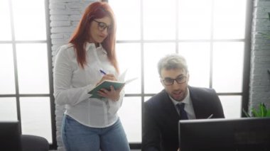 Modern bir ofiste iş birliği yapan iş adamı ve iş kadını dizüstü bilgisayar ve defterle doğal ışık altında bir proje üzerinde çalışıyorlar.