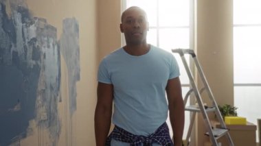 Genç adam aydınlık evin içini merdiven aletleri ve neşeli ifadeyle boyuyor.