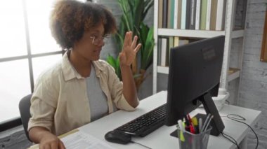 Büroda çalışan, bilgisayarında kıvırcık saçlı bir kadın, odak ve nişanı büyük pencerelerin yakınındaki bir masada gösteriyor ve ofis malzemeleriyle çevrili..