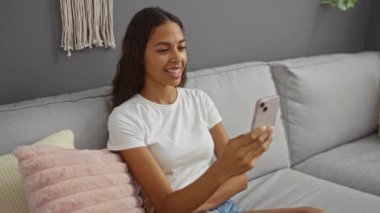 Oturma odasındaki bir kanepede otururken akıllı telefondan konuşan genç bir kadın.