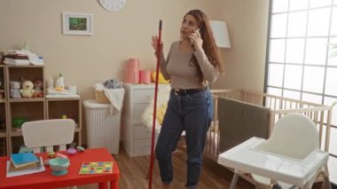 Bebeğin yatak odasını temizlerken telefonla konuşan bir kadın oyuncaklarla ve beşikle dolu, rahat bir ev ortamının altını çiziyor..