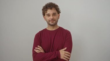 Mutlu bir gülümseme ve izole edilmiş beyaz bir arka plan üzerinde serin bir güvenle duran İspanyol genç adam neşe ve pozitif enerji saçıyor.