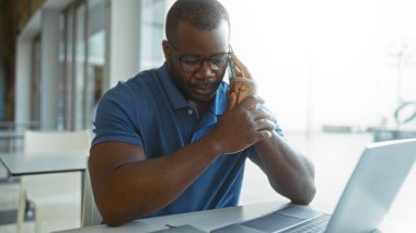 Bilgisayarla çalışırken ofiste telefonla konuşan genç bir adam.