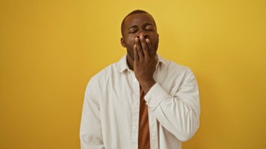 Yakışıklı genç adam izole edilmiş sarı arka plan duvarında esniyor yorucu bir jestle.