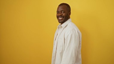 Yakışıklı, Afro-Amerikalı bir adam, izole edilmiş sarı arka planda gülümsüyor.