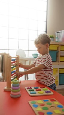 Küçük çocuk parlak bir anaokulu sınıfında eğitici oyuncaklarla oynuyor sarışın çocukluk aktivitelerini sergiliyor ve kapalı bir ortamda erken öğrenmenin önemi