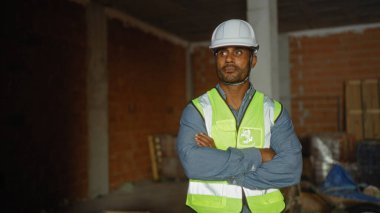 İnşaat alanında güvenlik yeleği ve miğfer takmış, tamamlanmamış bir bina ortamında güven ve profesyonellik yayıyor..