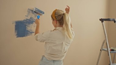 Yeni evde pateniyle duvar boyayan bir kadın oturma odasında iç dekorasyon projesi gösteriyor.