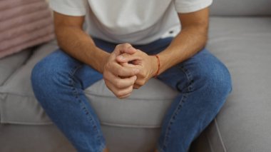 Evdeki gündelik bir odada elleri bağlı bir koltukta oturan Latin asıllı genç adam.