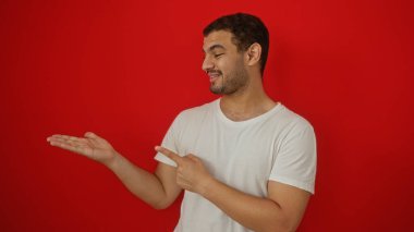 Genç bir adam, izole edilmiş kırmızı bir arkaplanı işaret ediyor ve açık bir elle sunuyor.