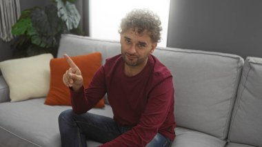 Rahat bir oturma odasında oturan bir adam, rahat bir kanepenin üzerinde minderlerle çevrili, kendinden emin bir ifadeyle tesadüfen yanlamasına duran bir adam..