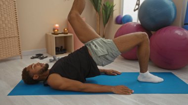 Genç adam spor salonunda hasırla egzersiz yapıyor. Spor aletleri, mumlar ve bitkilerle iç mekan hazırlıyor.