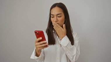 Kırmızı akıllı telefon kullanan genç bir kadın yatak odası ortamında şaşırmış görünüyor.