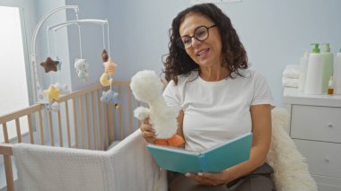 Yatak odasında beşikle kitap okuyan, sakin bir iç mekan ortamı sergileyen, İspanyol mirasını ve olgun zarafeti çevrende oyuncaklarla ön plana çıkaran bir kadın..