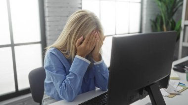 Modern ofiste eli yüzü bağlı bir kadın, bilgisayar masasında oturuyor, evrak işleriyle çevrili, kapalı bir çalışma ortamında ezilmiş hissediyor..