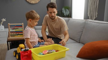 Baba ve oğul rahat bir oturma odasında oyuncaklarla ve abaküsle oyun oynuyorlar..