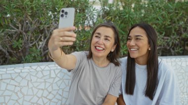Anne ve kızı parkta selfie çekiyorlar. Şehirdeki açık havanın tadını çıkarırlarken birbirlerine olan sevgilerini gösteriyorlar..