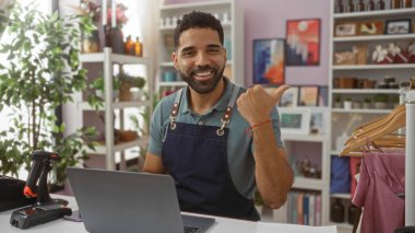 Genç adam arka planda bitki ve raflarla ev dekorasyonu dükkanında gülümseyen birini işaret ediyor.