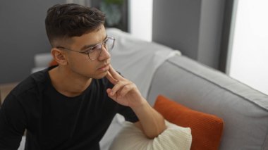 Evdeki oturma odasındaki bir koltukta gözlüklü genç İspanyol bir adam rahat bir iç mekanda çekici bir yetişkin erkeği sergiliyor..