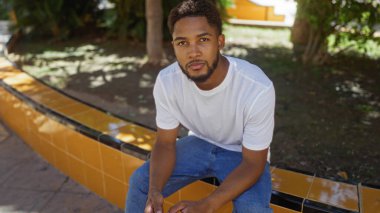 Güneşli bir günde şehir parkında oturan yakışıklı genç adam.