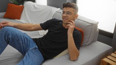 Genç İspanyol bir adam lüks bir oturma odasında rahat bir iç dekorasyonla rahat ve davetkar bir iç dekorasyon sergiliyor..