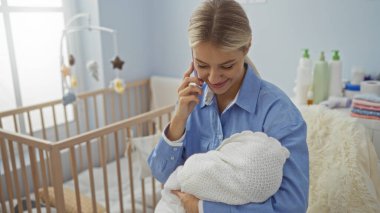 Beşikle süslenmiş, rahat bir yatak odasında telefonla konuşurken kucağında bir anne ve yeni doğmuş bir bebekle evde huzurlu bir anın altını çizen bir kadın..