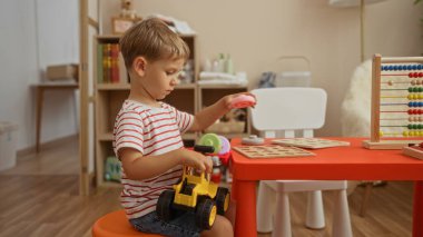 Etrafta abaküs ve eğitici bulmacalar olan sevimli bir anaokulu ortamında renkli bir masada oyuncaklarla oynayan küçük bir çocuk.
