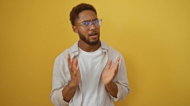 Gözlüklü yakışıklı genç adam. Parlak sarı arka planda izole edilmiş. Şaşırdığını ifade ediyor.