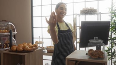 Pastanedeki İspanyol kadın, elinde eliyle müşterileri davet ederken, kafenin iç kısımlarında elinde hamur işleriyle tezgahın arkasında dikiliyor.