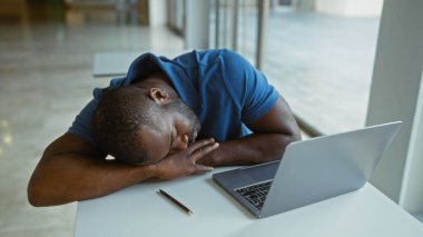 İş yerindeki bilgisayarın yanında uyuyan yorgun genç adam yorgunluk belirtileri gösteriyor.